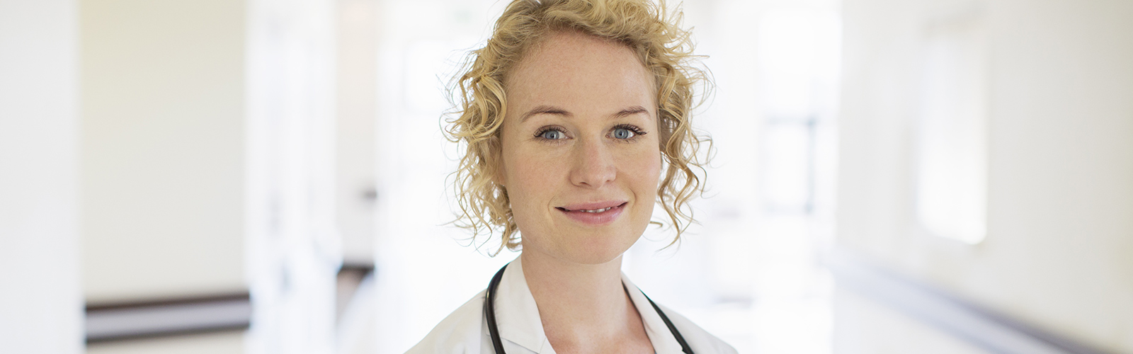 O doctoriță blondă cu stetoscop zâmbește pe holul spitalului O doctoriță blondă cu stetoscop zâmbește pe holul spitalului